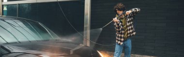 Araba yıkayan genç adam oto yıkama makinesinde, pankartta 