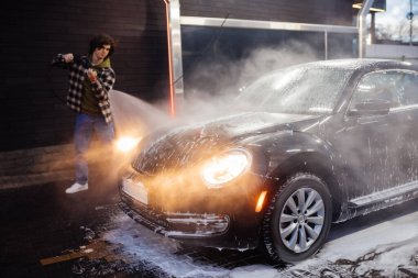 Car in foam near blurred driver with pressure washer outdoors  clipart