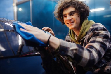 Smiling man in casual clothes cleaning car with rag on blurred foreground  clipart