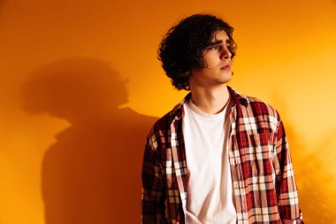 Üzgün kıvırcık adam turuncu arka planda gölgeye bakıyor. 