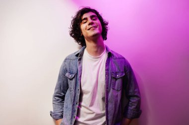 Kot gömlekli gülümseyen adam beyaz ve mor arka planda kameraya bakıyor. 