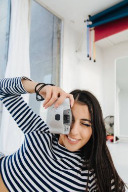 Çizgili kazaklı gülümseyen Ermeni kadın dijital kamerada fotoğraf çekiyor.