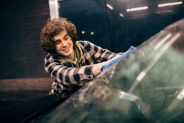 Young driver cleaning windshield with rag on self service car wash