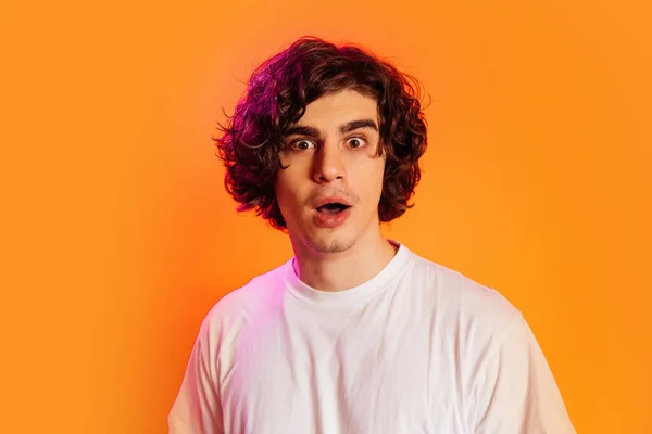 Mor ışıklı, turuncu üzerine izole edilmiş kameraya bakan hayran bir adam. 