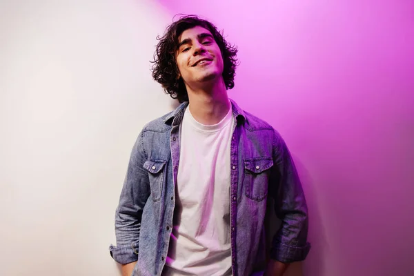 Kot gömlekli gülümseyen adam beyaz ve mor arka planda kameraya bakıyor. 