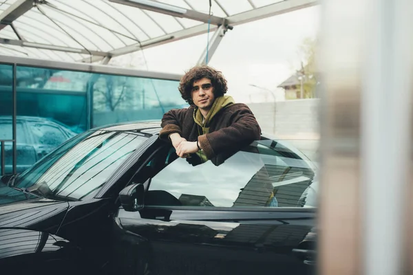 Young driver standing near car with open door on self service wash outdoors