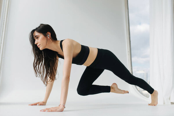 barefoot armenian woman practicing yoga in one-legged plank pose on white floor