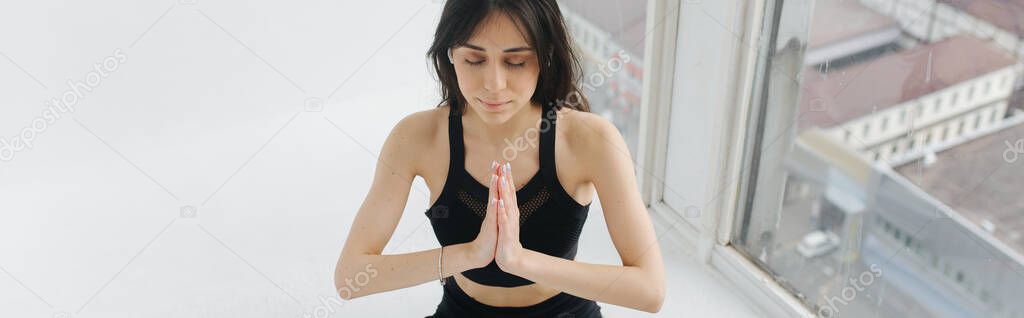sportive armenian woman meditating with praying hands near window, banner