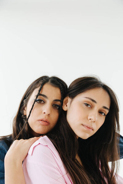 armenian woman leaning on shoulder of friend while looking at camera isolated on white