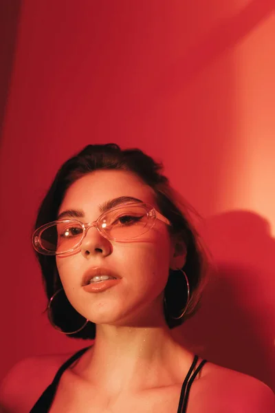 Портрет молодої жінки в сонцезахисних окулярах дивиться на камеру на червоному тлі — стокове фото