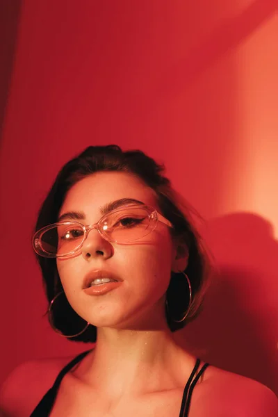 Portrait of young woman in sunglasses looking at camera on red background — Stock Photo