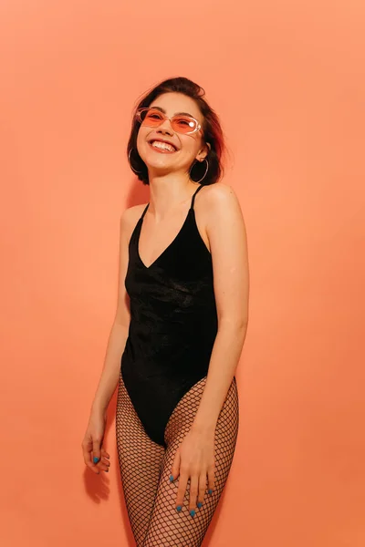 Heureuse jeune femme en body noir et lunettes de soleil posant sur fond orange — Photo de stock