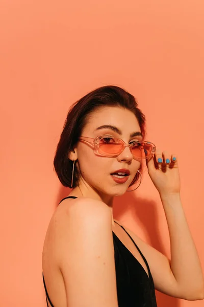 Junge Frau mit Sonnenbrille und halb geöffnetem Mund auf orangefarbenem Hintergrund — Stockfoto