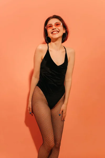 Smiling young woman posing in black bodysuit and fishnet tights on orange background — Stock Photo