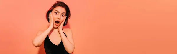 Aufgeregte junge Frau in schwarzem Tank-Top, die Hände vor dem Gesicht auf orangefarbenem Hintergrund, Banner — Stockfoto