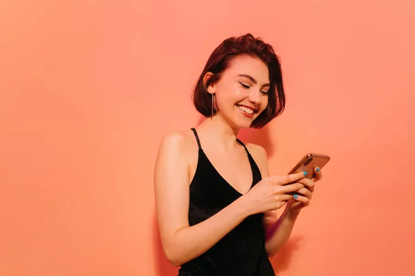 Щаслива молода жінка з мобільним телефоном в руках на помаранчевому фоні — стокове фото
