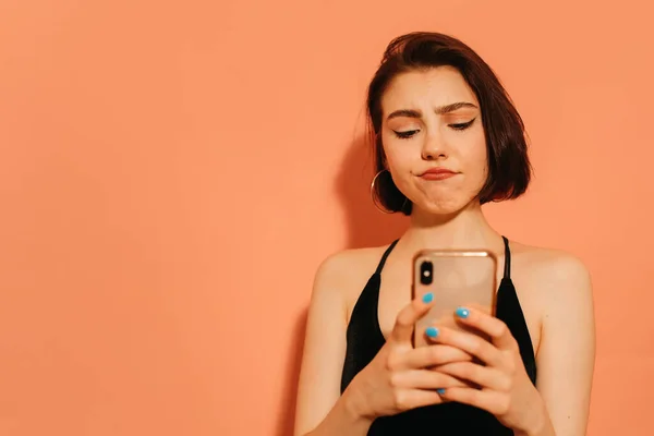 Молодая женщина смотрит на смартфон в руках на оранжевом фоне — стоковое фото