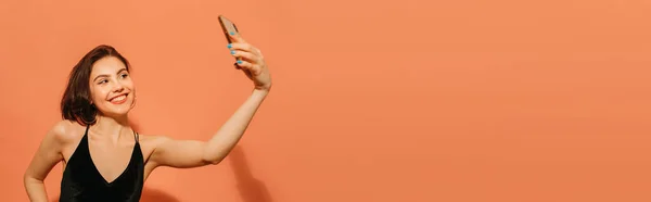 Giovane donna che prende selfie e sorride su sfondo arancione, striscione — Foto stock