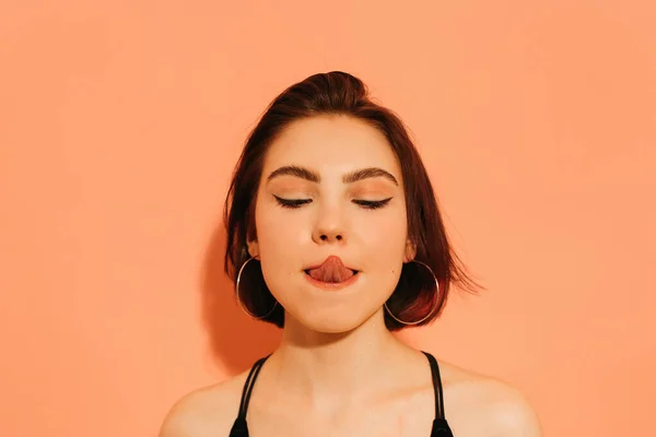 Young woman grimacing with sticking out tongue on orange background — Stock Photo