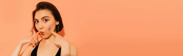 Mujer joven haciendo muecas con los labios y las manos de pucheros cerca de la cara sobre fondo naranja, pancarta — Stock Photo