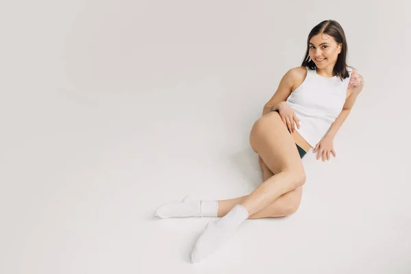 Relaxed young woman in white top, socks and black panties lying on grey background — Stock Photo