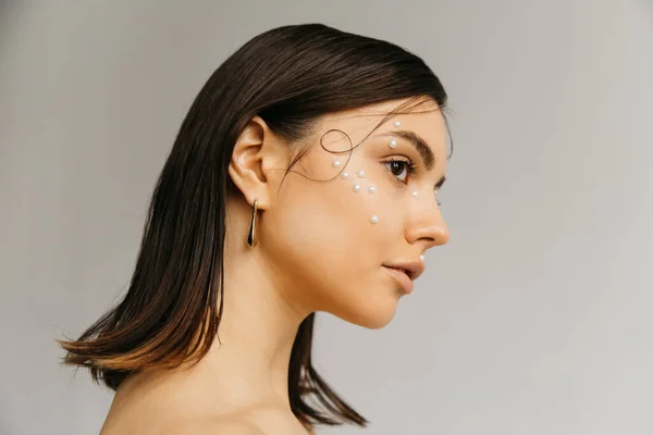 Vista laterale del viso giovane donna con pelle perfetta, trucco creativo e acconciatura isolata sul grigio — Foto stock