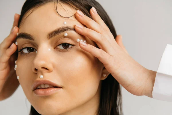 Retrato de manos de mujer joven cerca de la cara con maquillaje decorativo aislado en gris - foto de stock