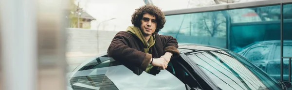 Curly man standing near car on self service car wash, banner — Stock Photo