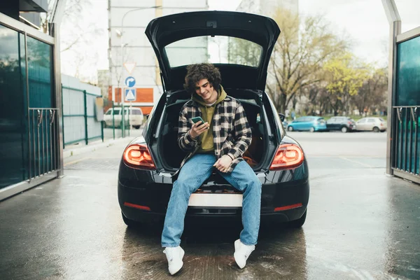 Smiling man using smartphone in auto trunk on self service car wash — Stock Photo