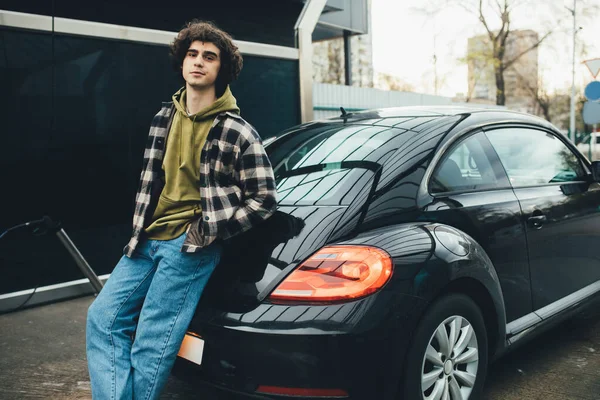 Lockiger Mann blickt auf Kamera in der Nähe sauberen Autos auf Selbstbedienungsautowaschanlage — Stockfoto