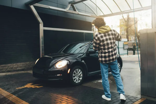 Vista trasera del hombre que sostiene la lavadora de presión cerca del coche al aire libre - foto de stock