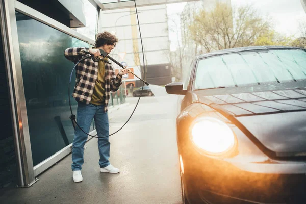 Seitenansicht eines lächelnden Mannes, der sein Auto auf einer Selbstbedienungswaschanlage wäscht — Stockfoto