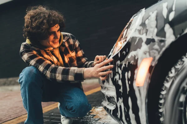 Smiling man looking at car in detergent on self service wash — Stock Photo