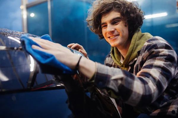 Uomo sorridente in abiti casual pulizia auto con straccio in primo piano sfocato — Foto stock