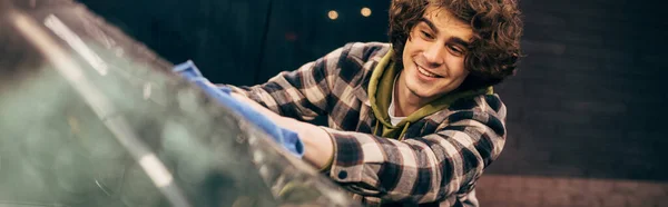 Smiling man cleaning windshield of auto on self service wash in evening, banner — Stock Photo