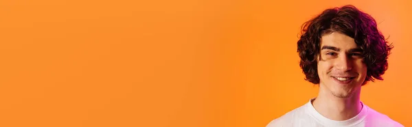 Fröhlicher Mann blickt in Kamera isoliert auf orange mit lila Beleuchtung, Banner — Stockfoto