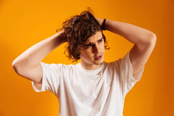 Young man adjusting curly hair on orange background — Stock Photo