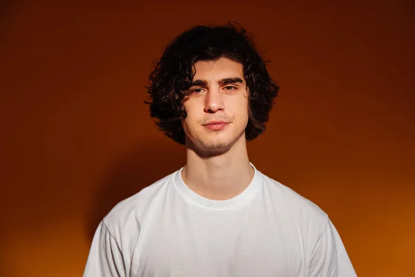 Junger Mann im weißen T-Shirt blickt in die Kamera auf braunem Hintergrund — Stockfoto