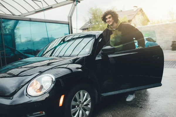 Lockiger Mann steht neben schwarzem Auto auf Waschstraße — Stockfoto