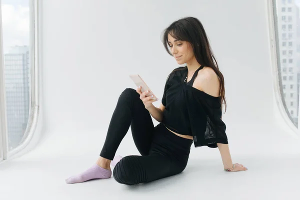 Pretty armenian woman smiling while sitting with cellphone on white floor — Stock Photo