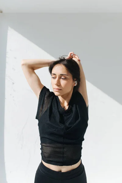 Femme arménienne rêveuse debout avec les mains derrière la tête près du mur blanc avec des ombres — Photo de stock