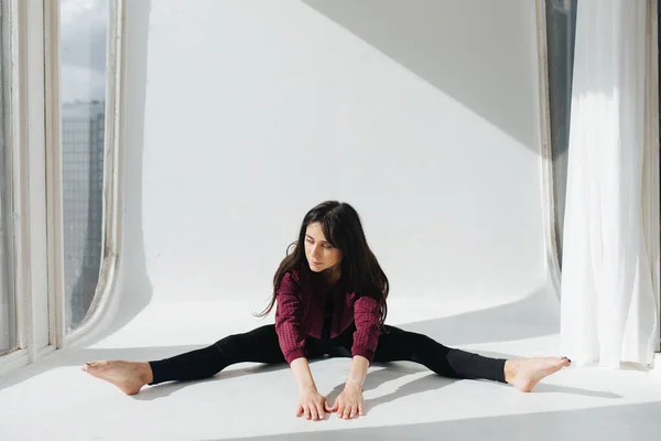 Barefoot armenian woman practicing wide-legged forward bend pose on floor near window — Stock Photo