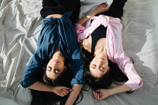 Overhead view of two armenian women in casual clothes sleeping on white bedding — Stock Photo