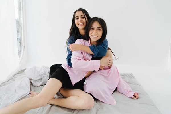 Couple of young and cheerful armenian women looking at camera while embracing in bedroom — Stock Photo