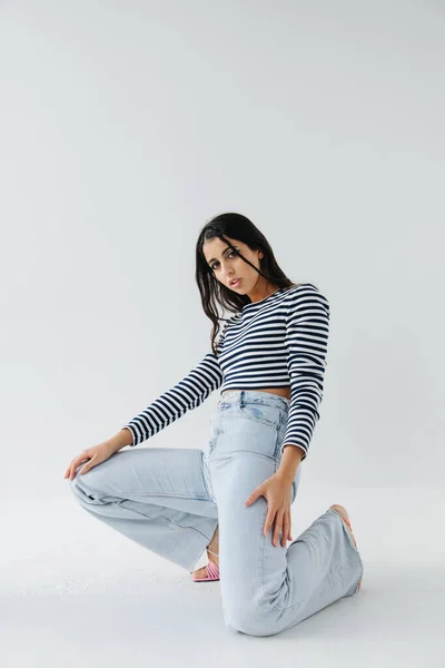 Pretty armenian woman in jeans and striped pullover posing on white background — Stock Photo
