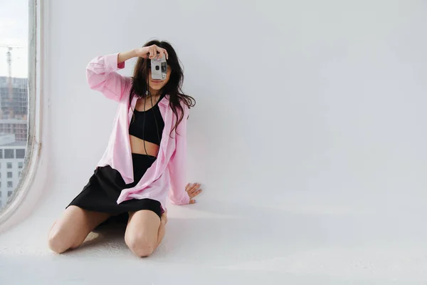 Young armenian woman in black top and mini skirt taking photo while sitting on white floor — Stock Photo