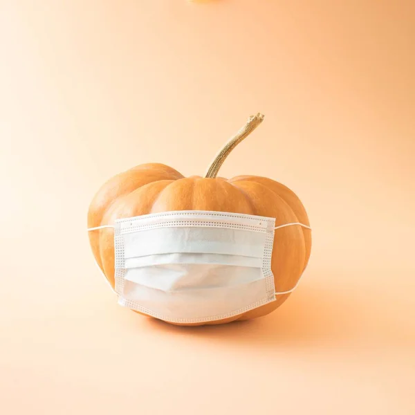 Pumpkin with a virus protection mask on a pastel orange background. Minimal layout.