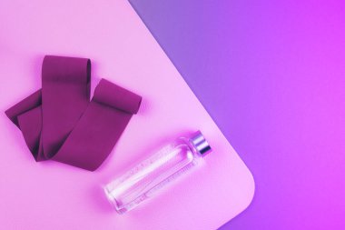 Neon mor ve pembe renkli kestane rengi genişletici elastik bant, pembe yoga minderiyle yeniden kullanılabilir cam su şişesi ve fotokopi alanı. Yoga, pilates, esneme ya da spor.. 