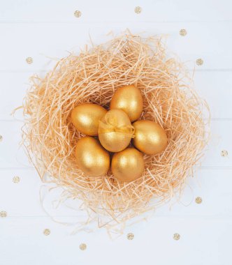 Beyaz arka planda dekoratif yuvada altın renkli Paskalya yumurtaları.