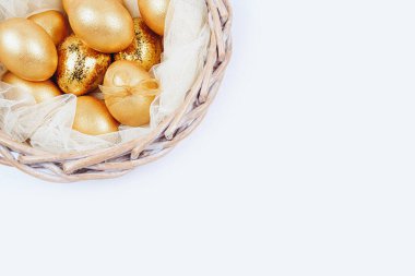 Hasır sepette beyaz arka planda altın renkli Paskalya yumurtaları. Boşluğu kopyala.